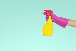 hand wearing purple rubber glove holding a bright yellow spray bottle