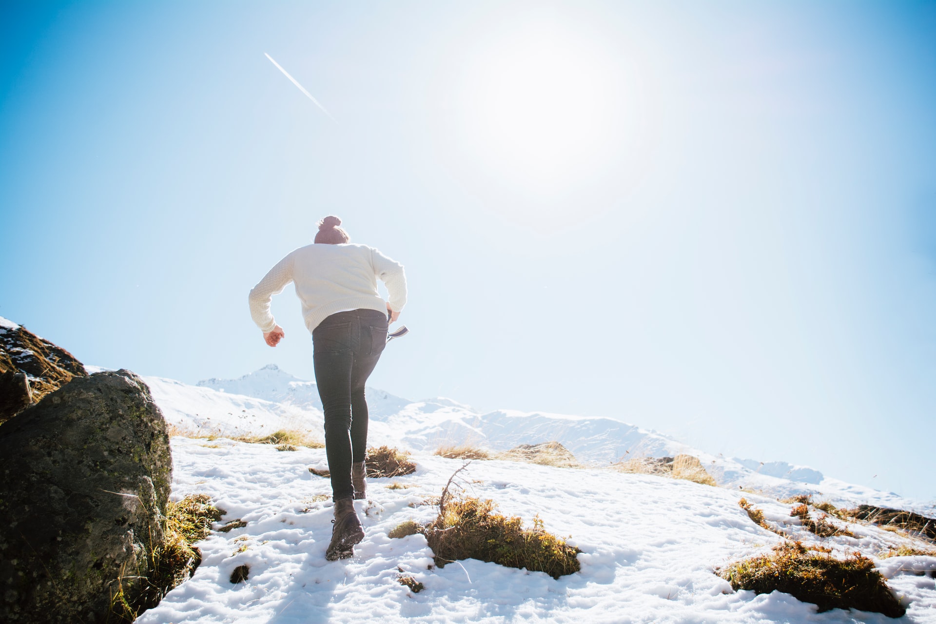 a person hiking up a snow topped mountain in jeans and a light sweater