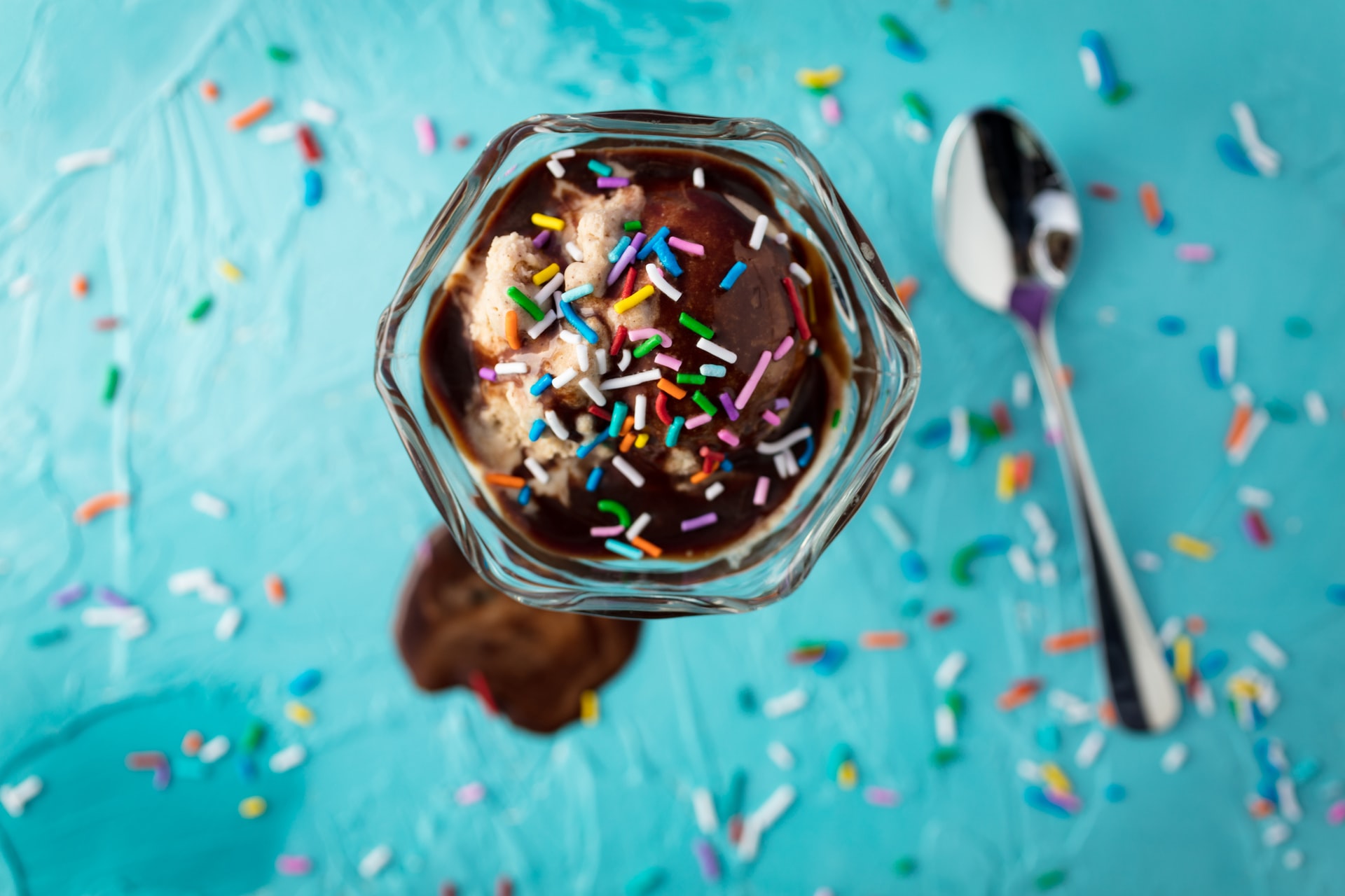 ice cream sundae topped with rainbow sprinkles next to a spoon