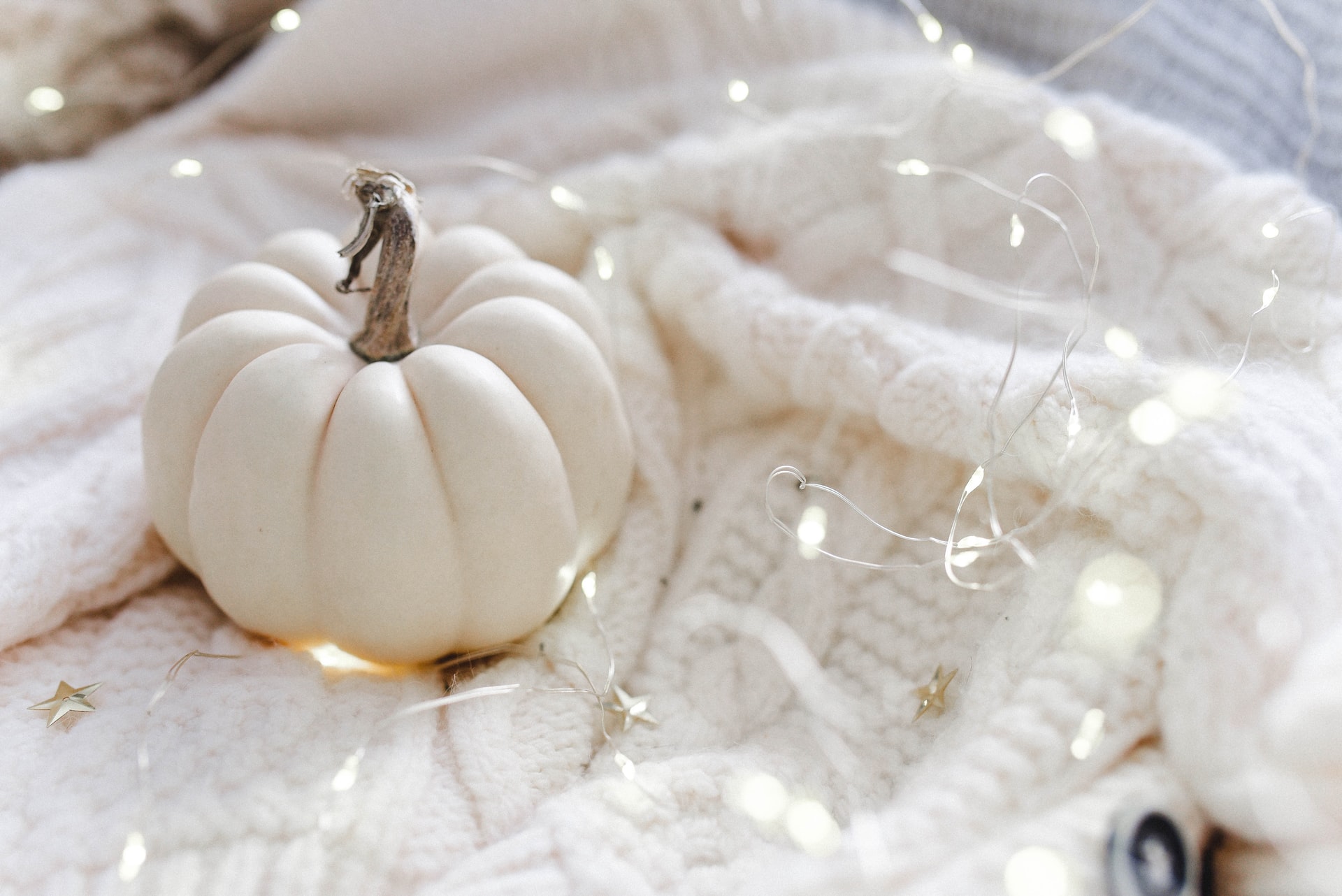 small white pumpkin sitting on a white cabled blanket surrounded by white fairy lights