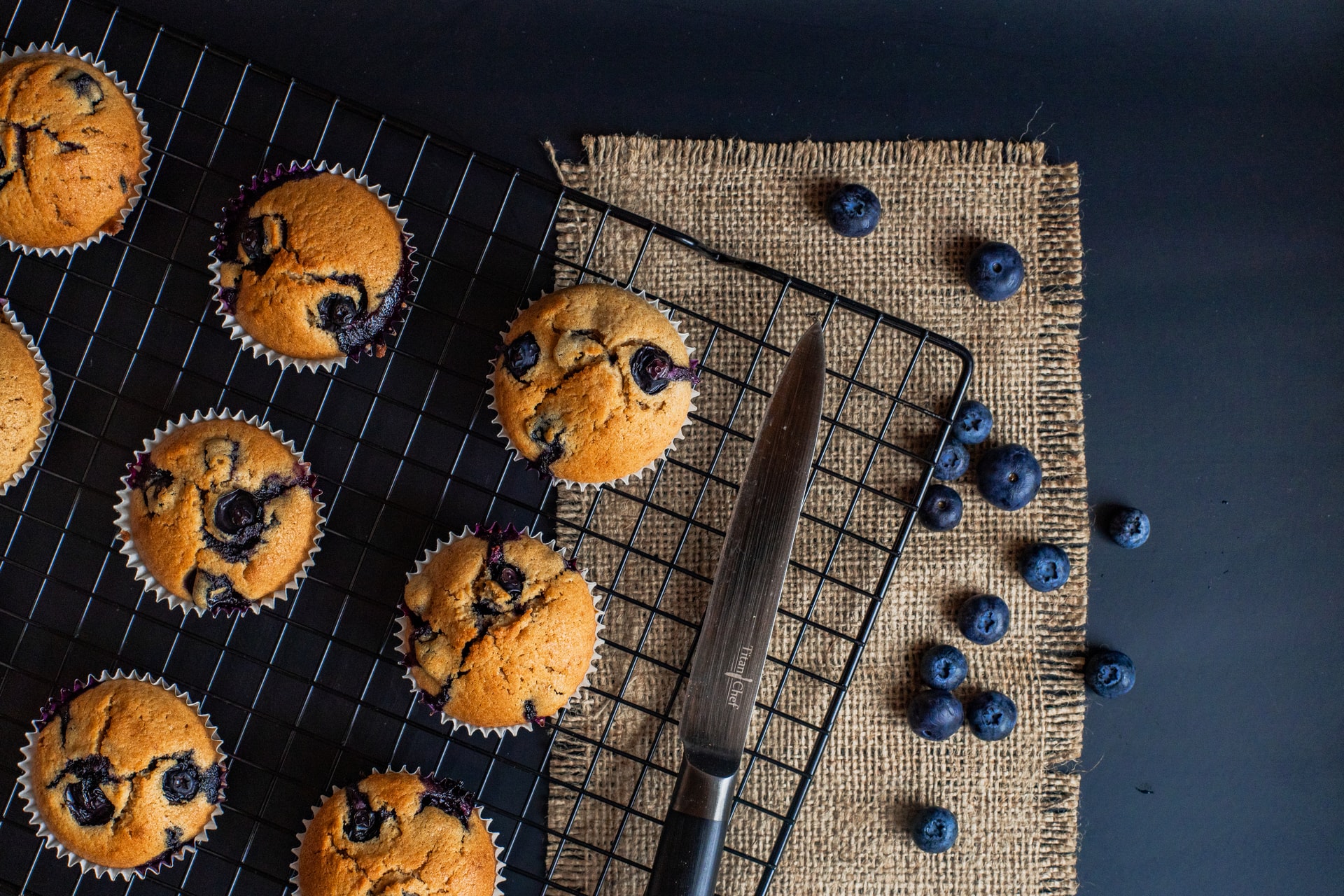 a cooling rack of blueberry muffins near a knife on a dark background