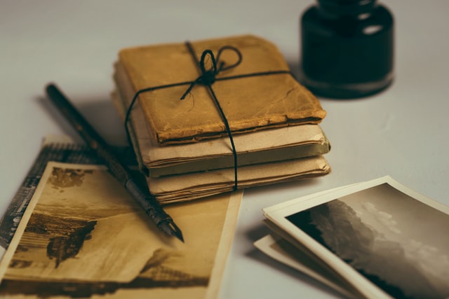 an antique parcel wrapped in black thread next to an ink pot, quill, and vintage photographs