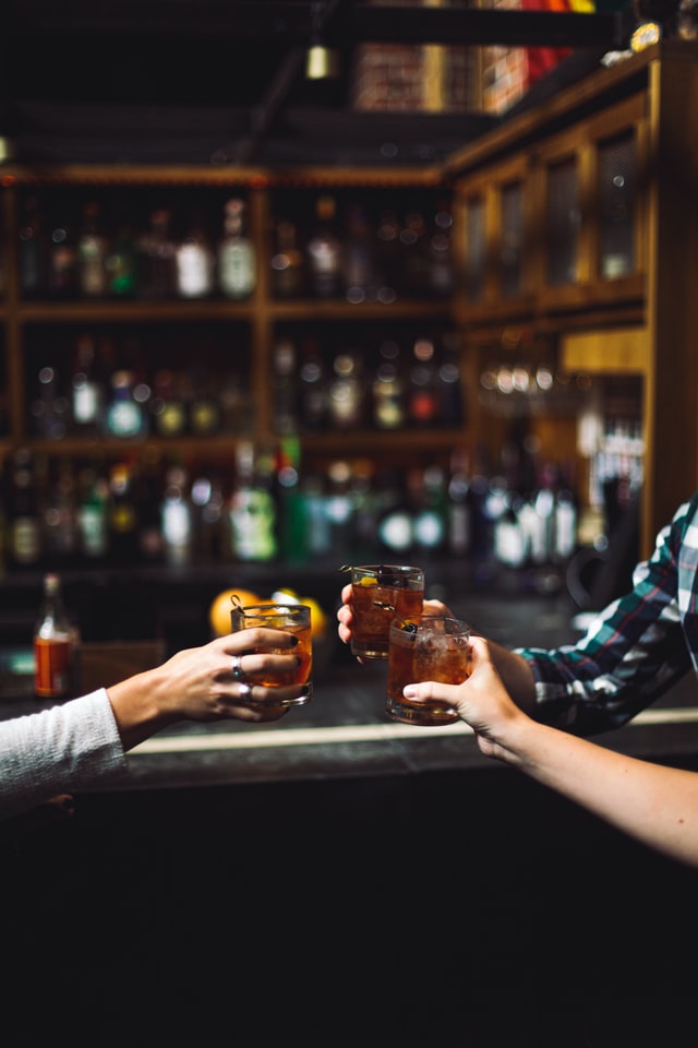 three people toasting glasses at a bar