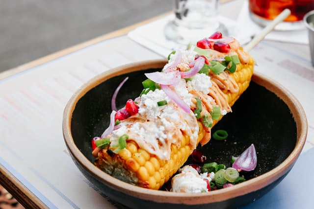 street corn on the cob topped with purple and green onions, and pomergranate seeds